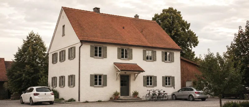 Das Wirtshaus von außen mit Vorplatz, Satteldach und Fensterläden